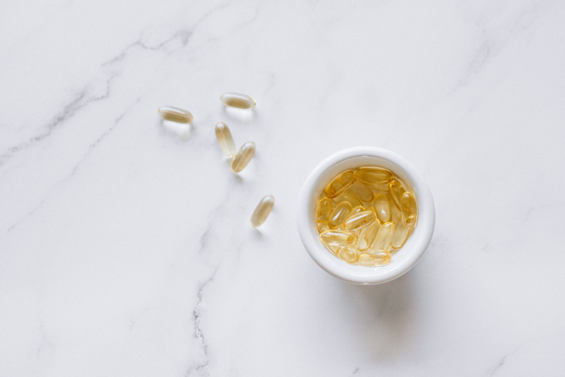 Omega 3 capsules (nutrition supplement) in a bowl and others outsid. Food date labels such as expiration dates on dietary/ nutritional supplements are critical for food safety.