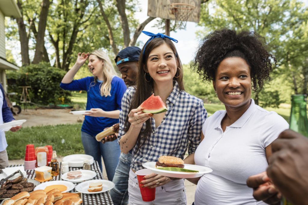 4 adults standing together happily as they get food for a BBQ. The risk of breast cancer is 1 in 8 for American women according to SEER Cancer Statistics Review submitted in 2019.